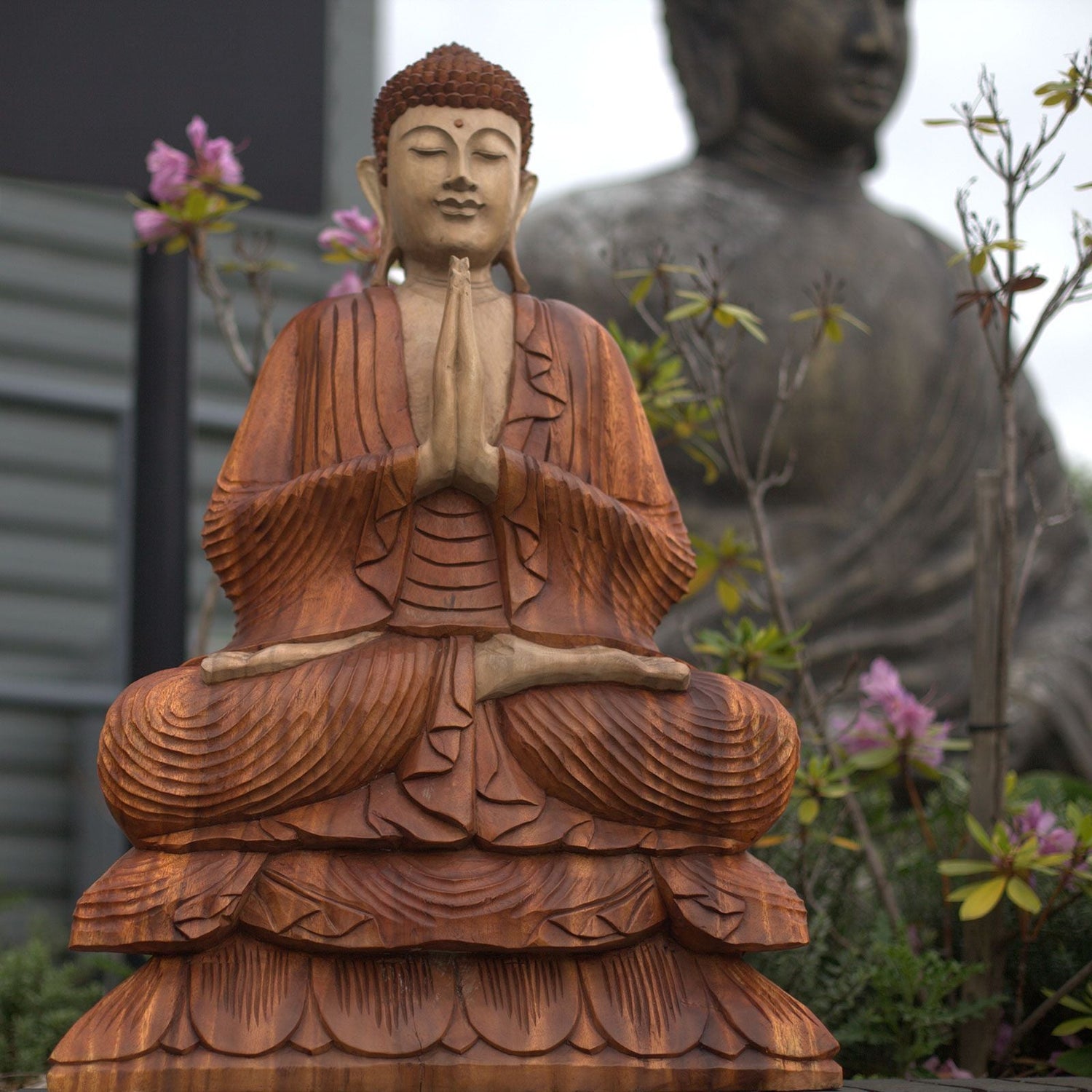Trois statues de Bouddha en bois sculpté, installées dans un jardin luxuriant avec bassin, représentant différentes postures méditatives dont le Bouddha Naga, un Bouddha en prière et un Bouddha couché, symbole de paix et de sérénité.